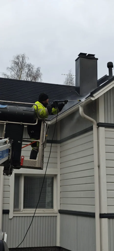Kiteen Kotihuollon työntekijä pesee katon reunaa ja kourua nostokorista.